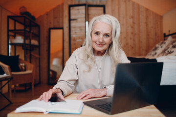 Mature Woman with laptop sitting at table and talking in glamping camping tent. Modern vacation lifestyle concept.