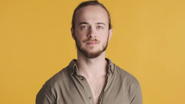 Young attractive bearded man dressed in casual wear looking confident on camera over yellow background. Face expression
