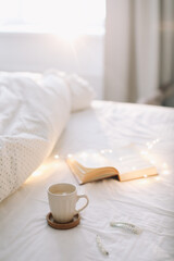 Fototapeta na wymiar Reading and having breakfast in bed. Coffee cup and a book in bed. Cozy sunny morning at home.