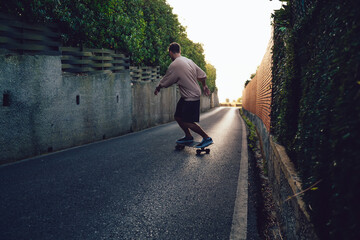 Rear view of skilled male skater practice freestyle on board on rural asphalt road during leisure time, young hipster guy enjoying practicing and spending weekends on active expreme hobby