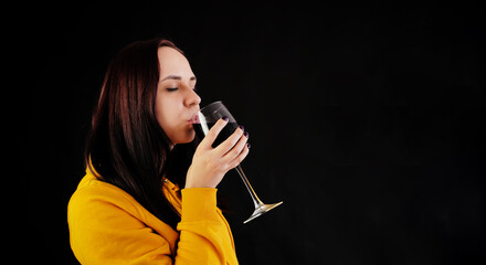 Relaxed young woman poses with glass of red wine on black background. Adult happy brunette resting with alcohol in her weekend.