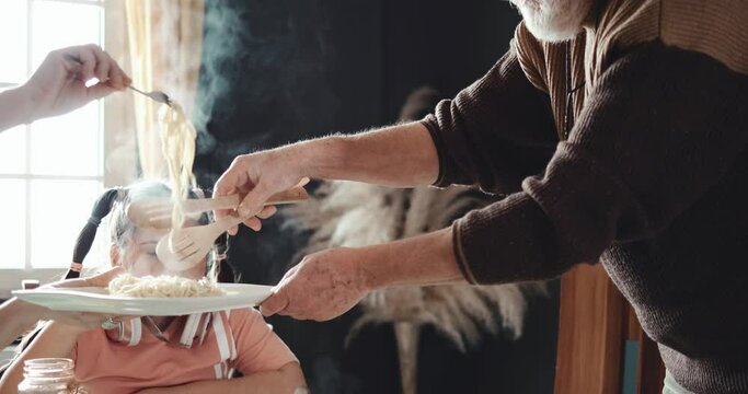 Hands of an old man with a gray beard pouring the pasta into a plate. Happy family hands. Grandparents eat in the kitchen
