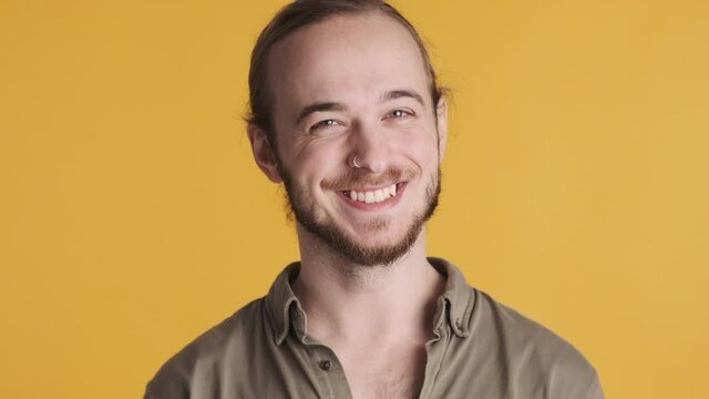 Handsome smiling bearded man looking happy agreeing on camera isolated on yellow background