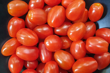 Closeup of a pile of cherry tomatoes in a black iron bowl.