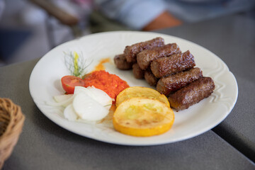 Delicious plate of Ćevapi, typical slovenian food served with yellow courgettes, onions, tomato and a spicy sauce.