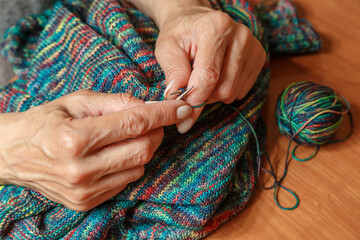 Close up of hands of unrecognizable woman knitting handmade clothes with spokes using  wool yarn. Concept of leisure activity.Knitting from yarn on  coarse spokes.