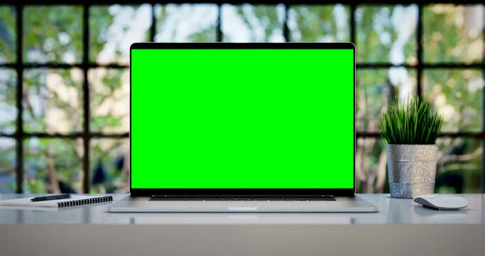 Laptop with blank green screen. Zoom in footage with trees swaying or moving in the wind. Home interior or loft office background, 4k 24fps UHD