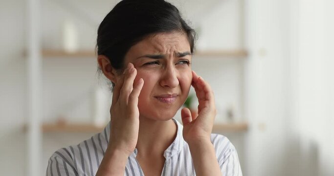 Unhealthy young 30s indian ethnicity woman massaging temples, stressed of having painful feelings, suffering from strong headache or severe migraine, first flu grippe covid19 symptoms concept.