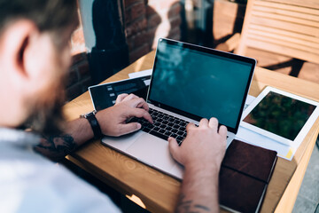 Male freelancer typing on laptop keyboard while working from outdoors cafe