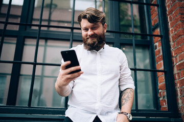 Obraz na płótnie Canvas Smiling man messaging on smartphone standing against window