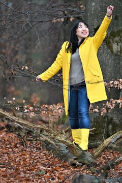 A woman in yellow raincoat and boots wandering in the wood 