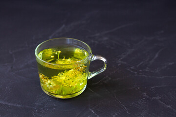 linden flowers tea.Cup of hot herbal tea with linden fresh flowers on a black table.Healthy lifestyle.glass cup of tea with green leaves on a black background.hot drinks.copy space. top view