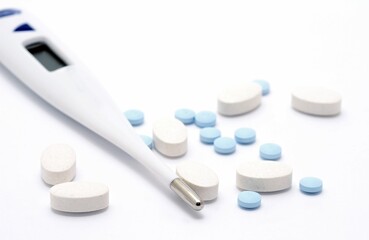 Pills and thermometer on white background