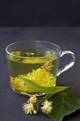 Close up linden flowers tea.Cup of hot herbal tea with linden fresh flowers on a black table.Healthy lifestyle.glass cup of green tea with leaves on a black background.hot drinks.vertical