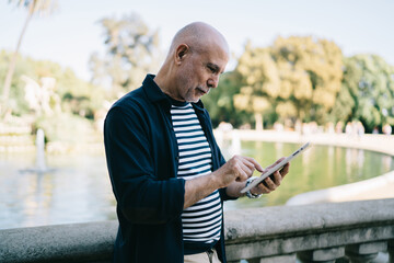 Fototapeta premium Caucasian male senior using 4g internet on modern gadget for reading network publication and make online booking, elderly man 60s checking received message newsletter during touch pad chatting