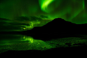 Raudasandur Mountain night shot northern lights circling above and reflecting in the water below