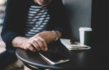 Unrecognizable male blogger checking time on modern cellphone gadget while resting in street cafe, cropped man using smartphone application for installing notification during wireless browsing