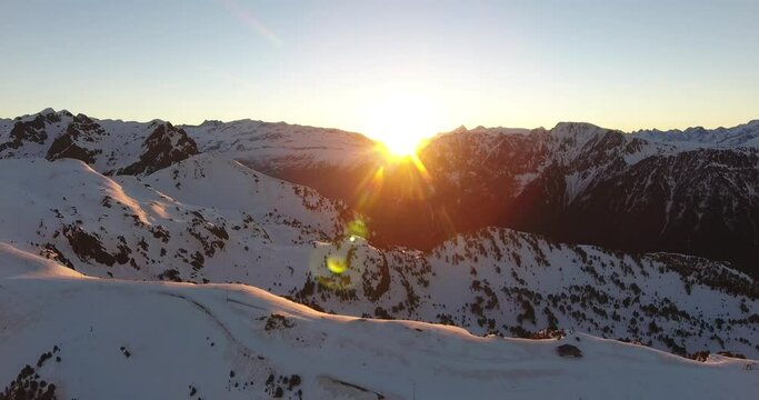 Sunrise at Chamrousse Alpine peaks in France with bright sun above ridge, Aerial dolly out