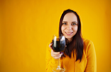 Relaxed young woman poses with glass of red wine on yellow background. Adult happy brunette resting with alcohol in her weekend.