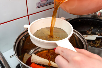 The woman pours the decoction of the mushroom soup through a plastic strainer.