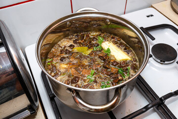 Mushroom soup with vegetables boiled in a metal pot on a gas stove.