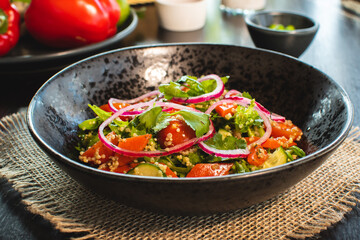 Quinoa salad with tomatoes, avocado, paprika and parsley on black stone plate.