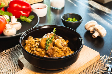 Pearl barley risotto or orzotto with mushrooms in dark bowl on wooden background. Selective focus.
