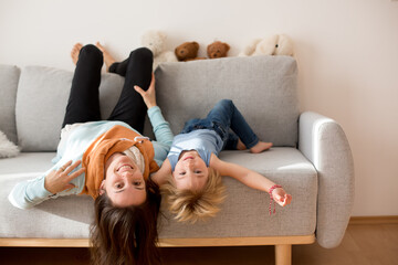 Mother and toddler child, hanging upside down from a couch at home, smiling