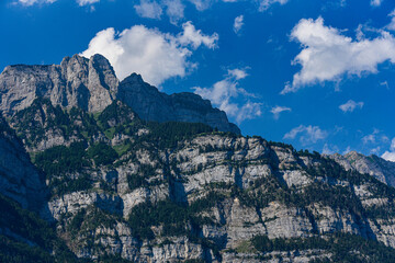 Fototapeta na wymiar Wooded steep mountainsite below a blue cloudy sky in Switzerland.