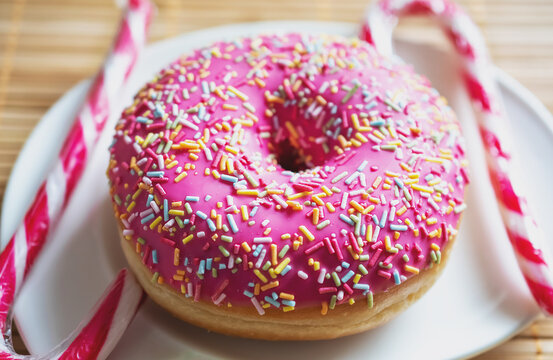 macro photo of a donut under pink glaze with multi-colored sprinkles