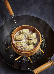 Gyoza dumplings steaming in a bamboo steamer over a wok pan.