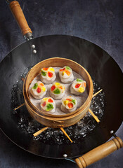 Sei Hei Gau (four seasons) dumplings steaming in a bamboo steamer over a wok pan.