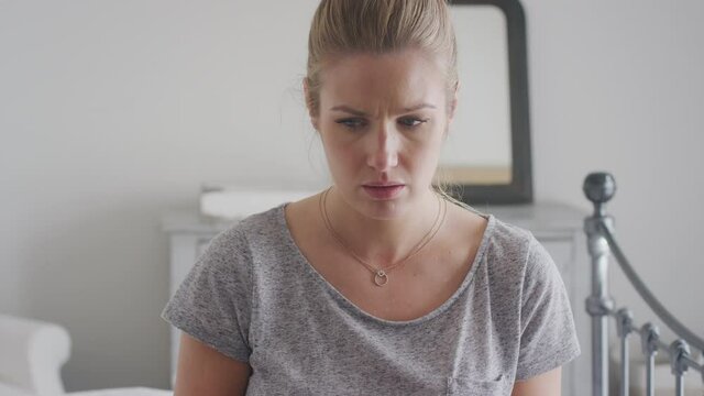 Unhappy woman wearing pyjamas sitting on bed with mobile phone being bullied online via social media and crying - shot in slow motion