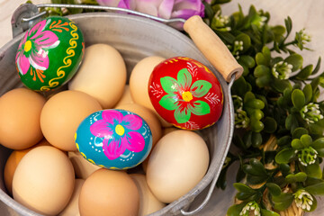 Natural color chicken eggs from the Easter decoration. In the center, a hand-painted Easter egg. Flower ornaments on the outside. All on a wooden background.
