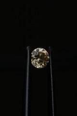 Yellow moissanite in tweezers on a black background