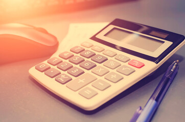 Calculator, pen, computer lie on the desk. Tinted photograph.