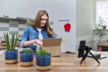 Woman recording video on smartphone unpacking cardboard box. Pet parrot helping to unpack