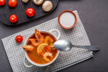 Tom yam soup with shrimps in a plate on the table on a napkin next to mushrooms and tomatoes.