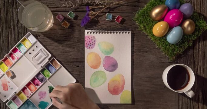 Happy Easter time-lapse – Asian woman painting a card of colorful Easter eggs with watercolor on wooden tabletop, morning time. Easter Holidays preparation at home. Handcraft and art work concept.