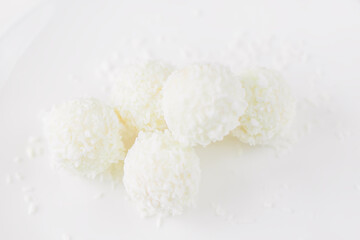 Food photography of natural vegetarian raw food candies with coconut. Close-up white round coconut candy on a white, delicate and airy background. Empty space for text. Flat lay top-down.