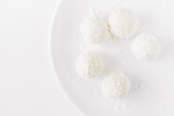 Obraz na płótnie Canvas Food photography of natural vegetarian raw food candies with coconut. Close-up white round coconut candy on a white, delicate and airy background. Empty space for text. Flat lay top-down.