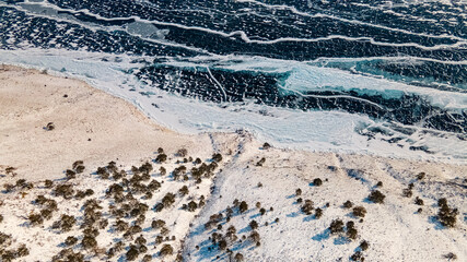 Frozen Lake Baikal top view. Ice, cracks, snow, shore, trees. Irkutsk region, Russia