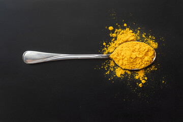 Yellow turmeric slide is in the metal spoon . Black background. Spice. Seasoning for dishes.