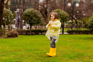 Fototapeta premium a beautiful girl in a yellow raincoat with a hood,and yellow boots, walks in the park with her favorite dog of the Russian spaniel breed