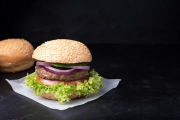 Tasty burger on the black background, delicious cutlet and sesame bun.