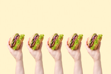 Many female hands with delicious burgers on a yellow background.