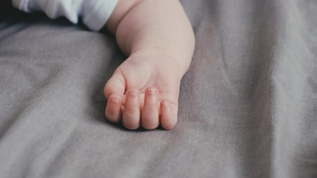 Close up of tender little infant child baby kid hand with five fingers lying on cozy grey bed at home. Baby skincare concept