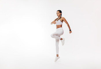 Young fit woman exercising over white background. Female in white sportswear jumping indoors.