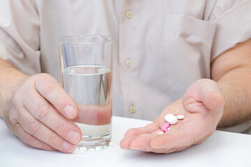 Taking pills, a glass of water in the hand of an elderly person.