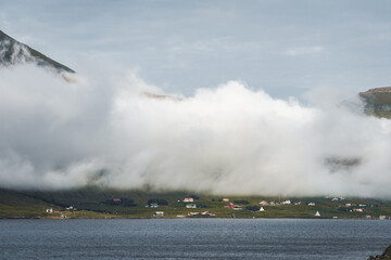 Spectacular views of clouds and fog covering the scenic fjords on the Faroe Islands on the island ov Vagar during a sunny day with blue sky.